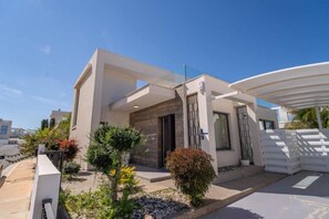 A modern two-story house with a flat roof, a covered patio, and a well-maintained garden. - Panorama Luxury Summer Villa (Paralimni)