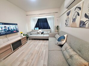 Ein Wohnzimmer mit einer Couch, einem Fernseher und einem Fenster mit Vorhängen.