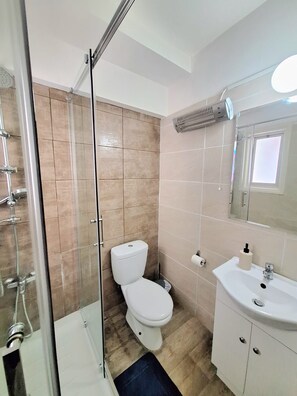 Ein Badezimmer mit Duschkabine aus Glas, Toilette, Waschbecken und Spiegel.