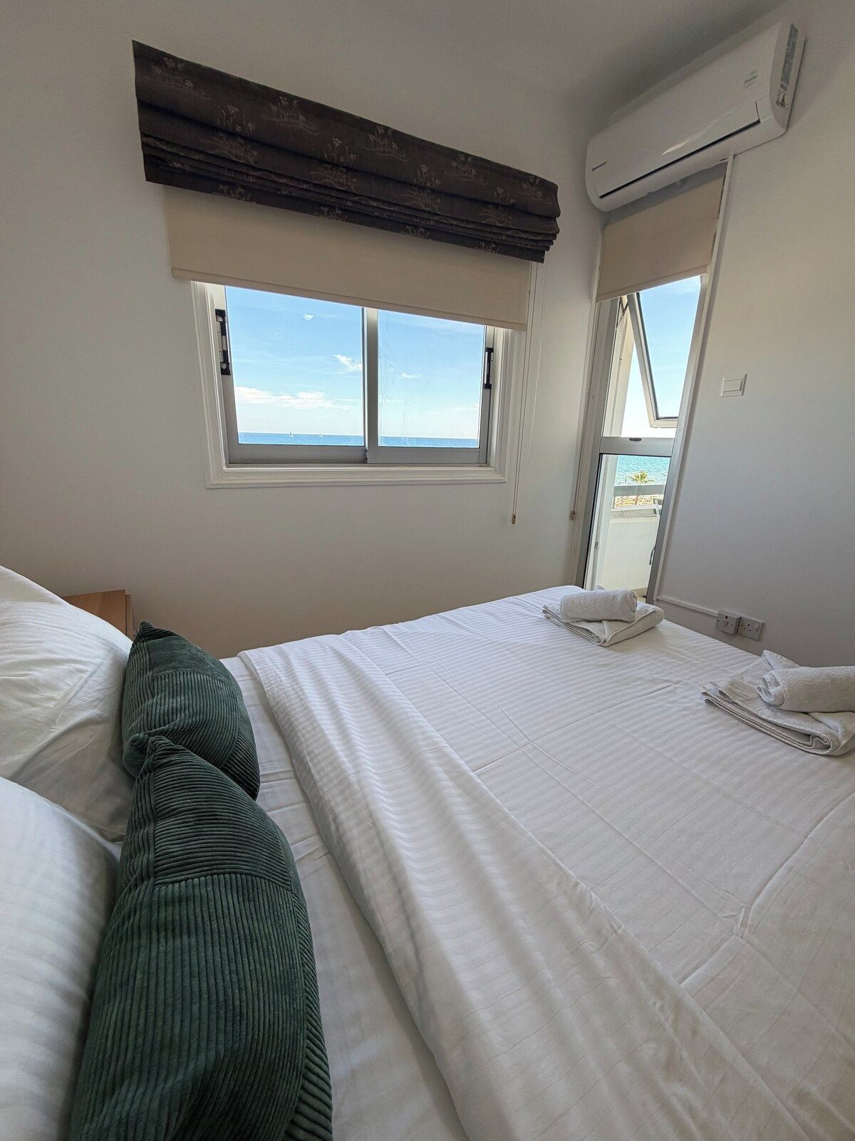 A hotel room with a bed, a window with a view, and an air conditioning unit.