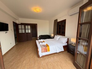 Ein Hotelzimmer mit einem großen Bett, einem Nachttisch, einem an der Wand befestigten Fernseher und einer Holztür mit Glaseinsätzen.