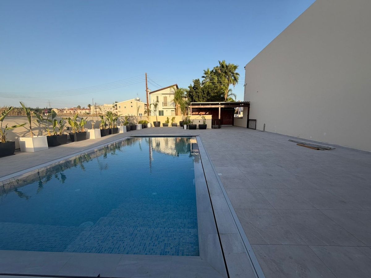 A swimming pool with a clear blue water surface, surrounded by a paved deck.