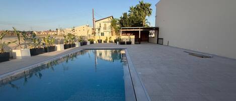 A swimming pool with a clear blue water surface, surrounded by a paved deck.