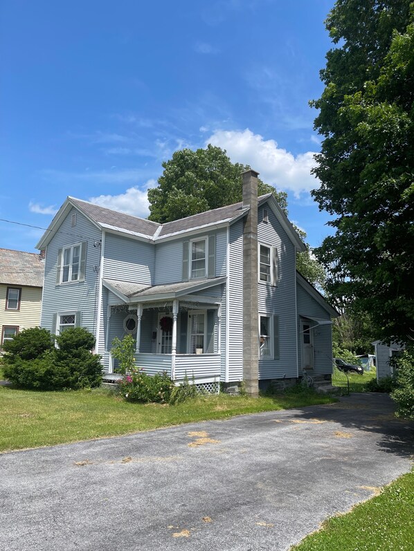 A two-story house with a porch, a chimney, and a driveway. - Bright and Cheery 3 Bedroom Home w/Wifi and Laundry (Poultney)