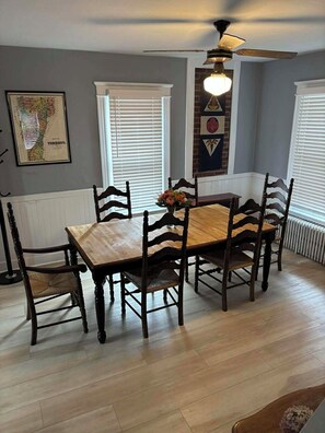 A dining area with a wooden table and chairs, a ceiling fan, and a framed map on the wall. - Bright and Cheery 3 Bedroom Home w/Wifi and Laundry (Poultney)