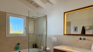 Een moderne badkamer met een douchecabine van glas, een grote spiegel, een bad en een toilet.
