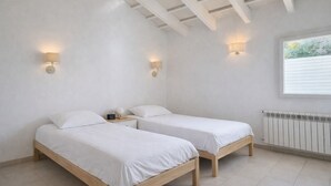 Een kamer met twee eenpersoonsbedden, een houten vloer, witte muren en een raam met jaloezieën.
