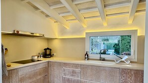 Een moderne keuken met een ingebouwde kookplaat, een raam met uitzicht op groen en houten keukenkastjes.