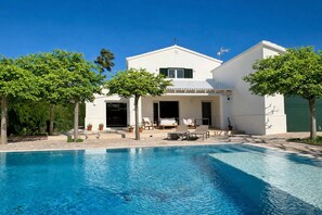 Et moderne hus med swimmingpool, udendørs møbler og en have.