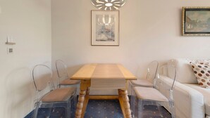 A dining area with a wooden table, clear chairs, a ceiling light fixture, a framed picture, and a white sofa with a polka dot pillow.