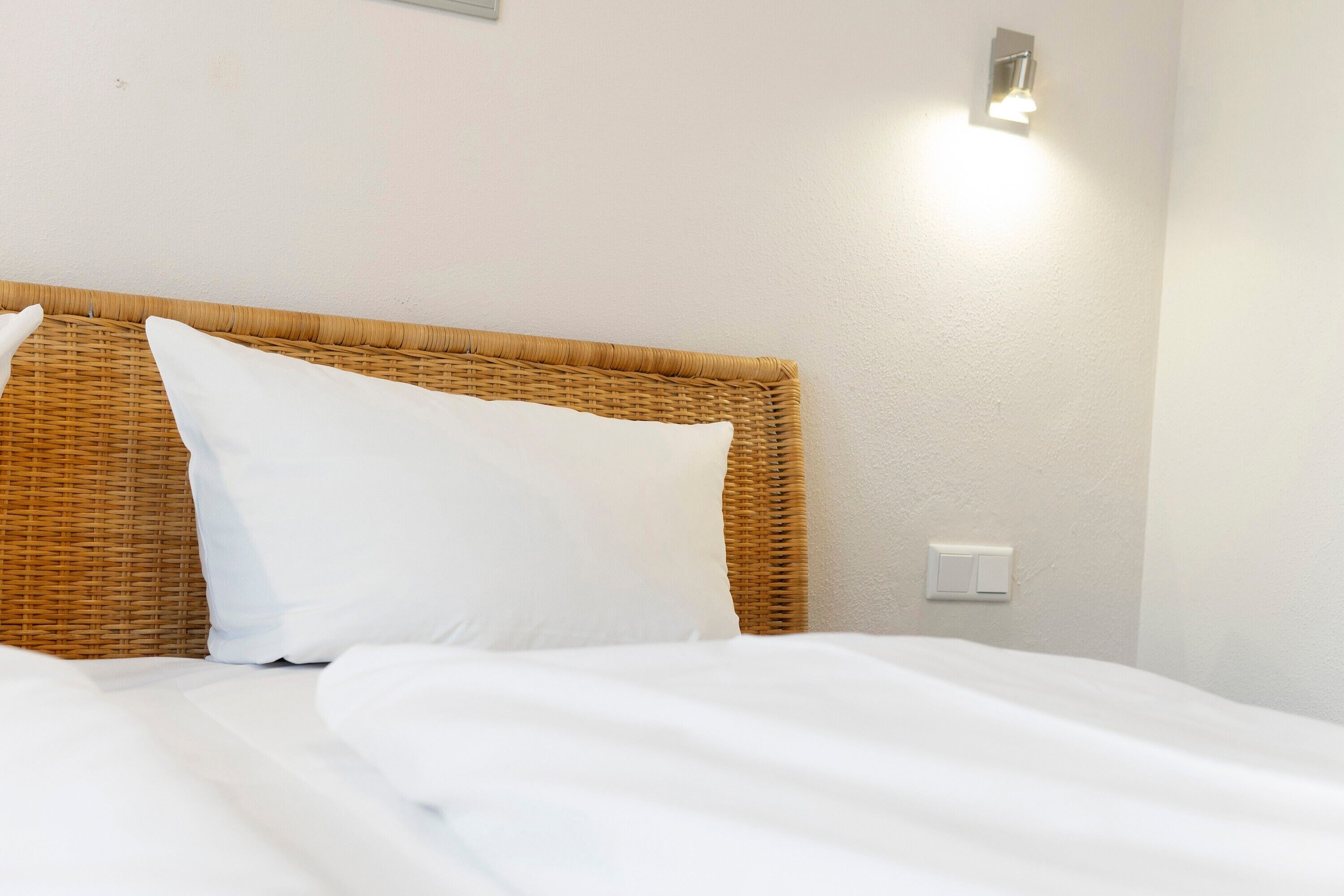 Een bed met wit beddengoed en een rieten hoofdbord.