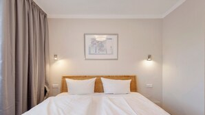 A hotel room with a large bed, two wall-mounted lights, a framed picture on the wall, and a window with curtains.