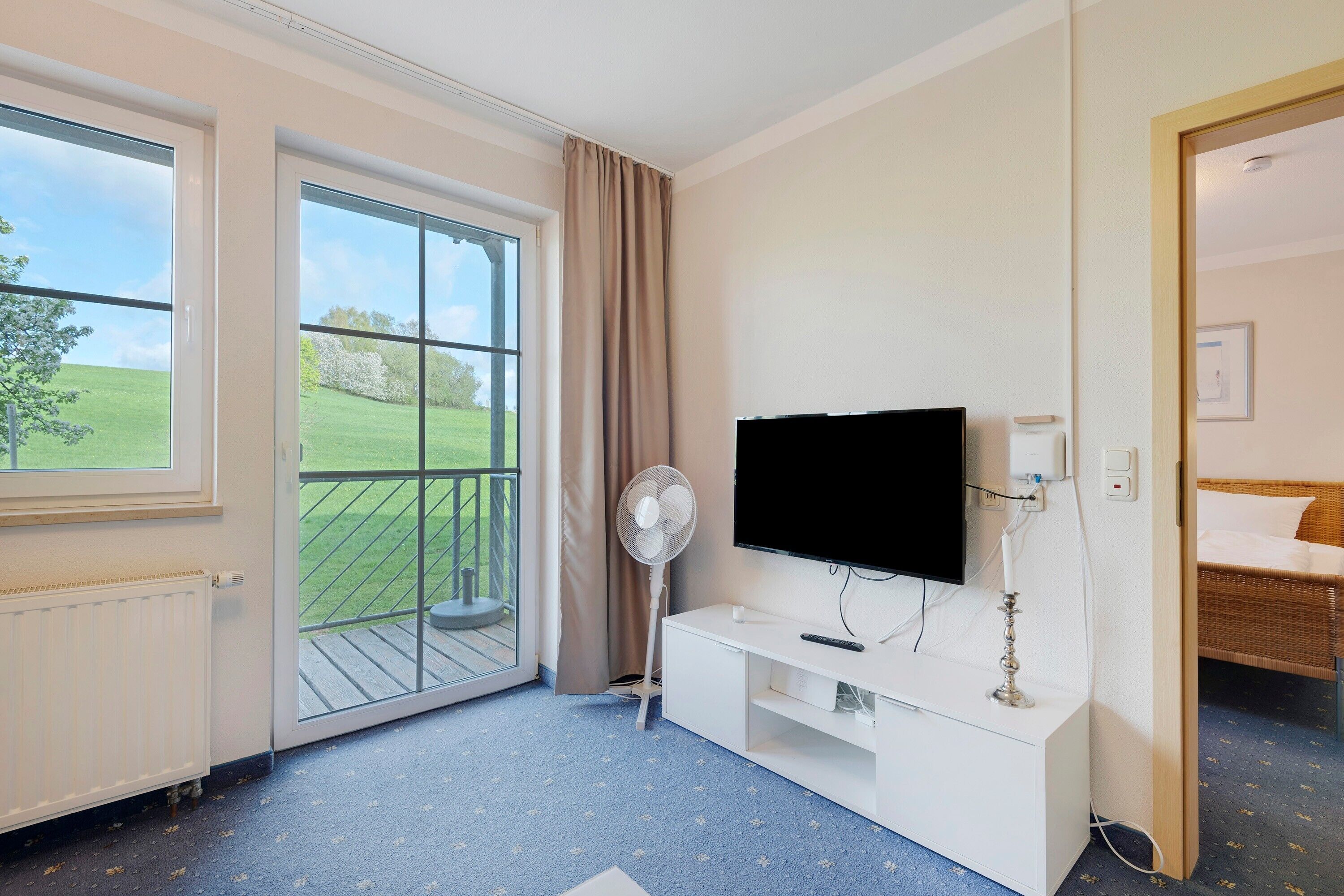 A room with a large window, a flat-screen TV, a white cabinet, and a balcony.