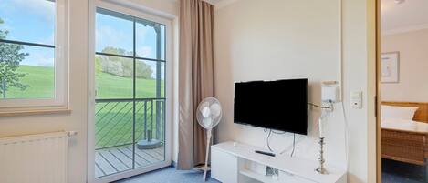 A room with a large window, a flat-screen TV, a white cabinet, and a balcony.