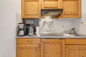 Une cuisine avec des meubles de rangement en bois, une bouilloire en acier inoxydable, une machine à café et une hotte aspirante.