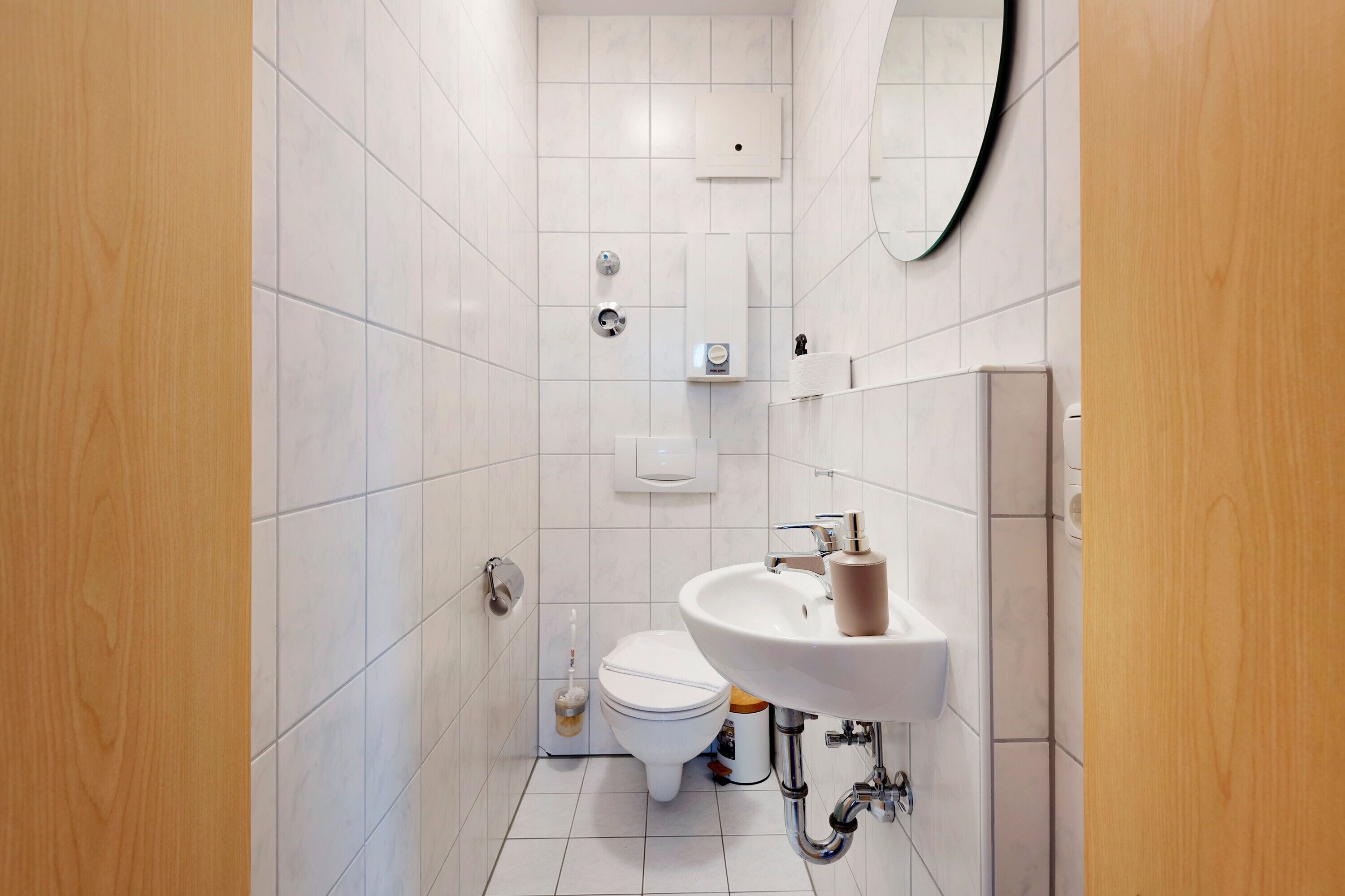 Une salle de bain moderne avec des carreaux blancs, des toilettes, un lavabo et un miroir.