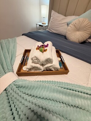 A neatly made bed with a blue and white striped bedspread, a white pillow, and a wooden tray holding folded towels and a small decorative item. - Blue ocean
First-floor two-bedroom apartment (Santo Domingo Este)