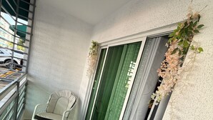Un balcón con dos sillas blancas y una cortina verde.
