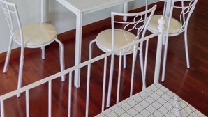 Ein Essbereich mit einem weißen Tisch und Stühlen, einem Fenster mit grünem Rahmen und einer Wandleuchte.