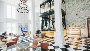 Een hotel lobby met zwart-wit schakkepad vloer, een bar en een zithoek met rieten stoelen.