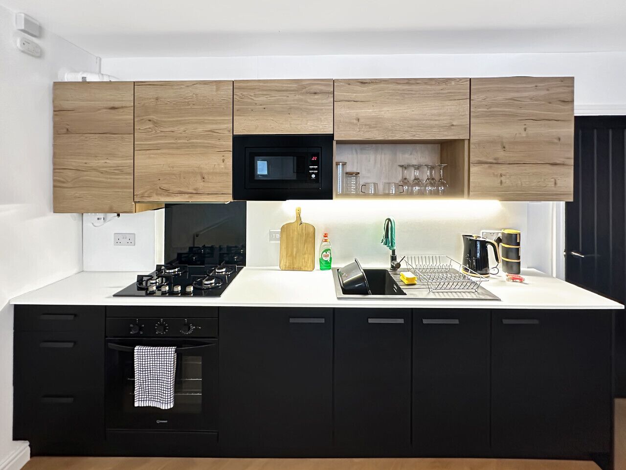 Une cuisine moderne avec des meubles de couleur noire, un four à micro-ondes, un évier avec un égouttoir et une cuisinière.