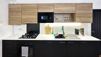A modern kitchen with black cabinets, a microwave, a sink with a dish rack, and a stove.