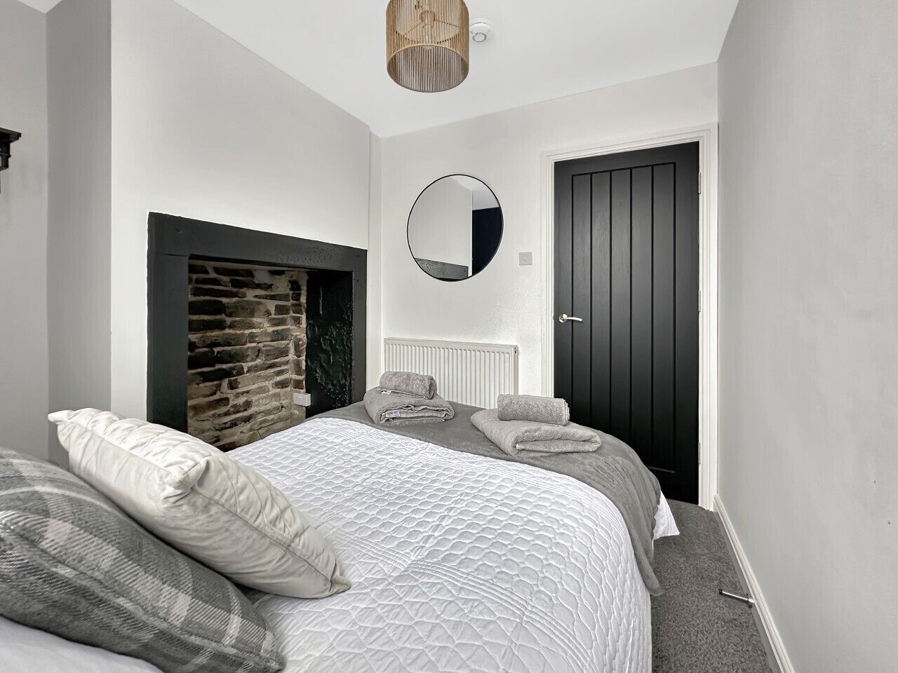Une chambre à coucher avec un lit, un miroir fixé au mur, une porte sombre et un mur en pierre.
