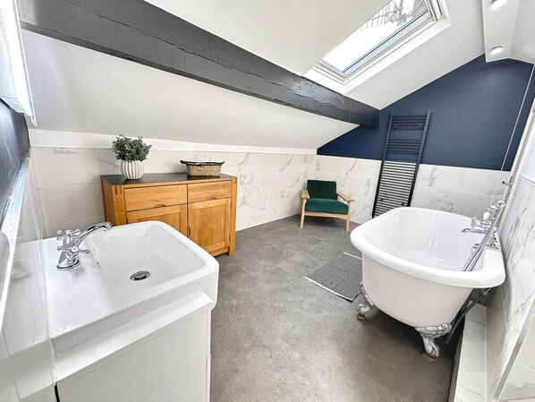 Une salle de bain moderne avec une baignoire sur pieds, un meuble-lavabo en bois et une chaise verte.