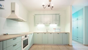 Une cuisine avec des armoires bleu clair, une hotte de cuisinière en acier inoxydable, un four double et un luminaire.