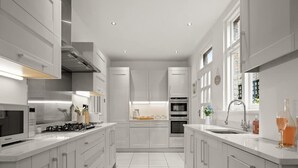 A modern kitchen with white cabinetry, a central island, a built-in oven, and a stainless steel range hood. - Relaxed Family Retreat in Kingston (Kingston Upon Thames)