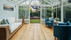 A conservatory with a glass ceiling, wicker furniture, and potted plants. - Relaxed Family Retreat in Kingston (Kingston Upon Thames)