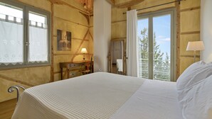 Une chambre dans une cabane en bois, avec un lit, un bureau, une chaise, une lampe et une fenêtre avec des rideaux.