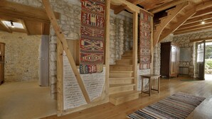 Un intérieur rustique avec un escalier en bois, des murs en pierre et une vue sur l’extérieur.