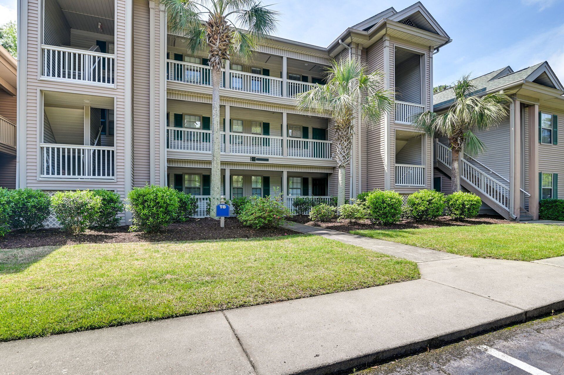 A multi-story hotel with balconies, a well-maintained lawn, and a clear sky.
