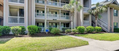 A multi-story hotel with balconies, a well-maintained lawn, and a clear sky.