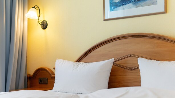 A neatly made bed with white linens, a wooden headboard, a wall-mounted light fixture, and a framed picture on the wall. - Apartment with Garden View (Spalt)