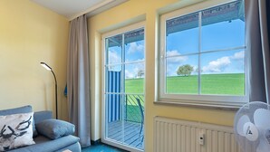 A room with a sofa, a standing lamp, a window with a view of a green field, and a radiator. - Apartment with Garden View (Spalt)