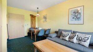 A room with a sofa, a dining table with chairs, a wooden door, and a framed picture on the wall. - Apartment with Garden View (Spalt)