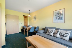 A room with a sofa, a dining table with chairs, a wooden door, and a framed picture on the wall. - Apartment with Garden View (Spalt)