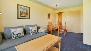 Ein Zimmer mit einer Couch, einem Esstisch mit Stühlen, einer Holzbank und einer Tür zu einem weiteren Raum.