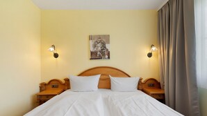 Ein Doppelbett mit weißen Bettlaken, zwei Nachttische, ein Holz-Kopfteil, ein an der Wand befestigtes Kunstwerk und zwei Wandleuchten.