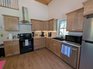 A kitchen with wooden cabinets, a stainless steel refrigerator, a microwave, a stove, and a sink. - Little Red Cabin on 60 Acres with private National Forest Access, pond, fire pit (Criders)
