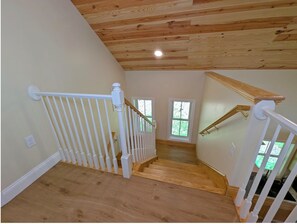 A wooden staircase with white railings, a ceiling with wooden beams, and a view of greenery outside. - Little Red Cabin on 60 Acres with private National Forest Access, pond, fire pit (Criders)