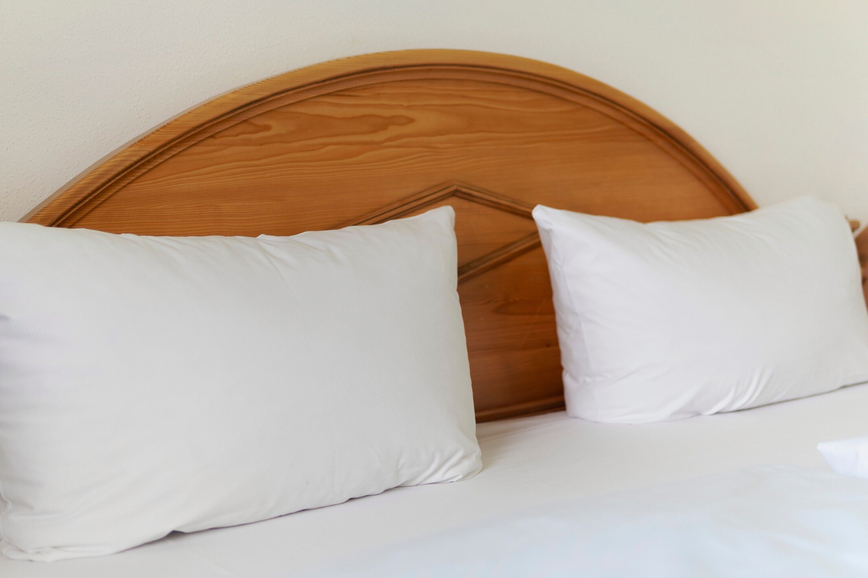 A bed with a wooden headboard and two white pillows.
