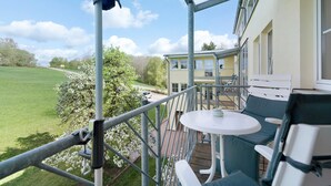 A covered outdoor area with a table and chairs, a view of a green field, and a building in the background. - Apartment with Garden View K1 206 (Spalt)