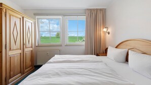 A bedroom with two beds, large windows, a wooden wardrobe, and a nightstand with a lamp. - Apartment with Garden View K1 206 (Spalt)