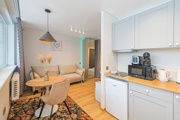 A compact living space with a kitchenette, a dining area with a table and chairs, a sofa, and a decorative vase with dried flowers.