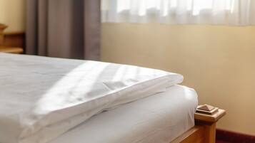 Una cama bien tendida con sábanas blancas, cabecero de madera y una ventana con cortinas traslúcidas.