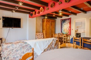A room with a bed, a dining table, chairs, a wooden cabinet, a television, and a kitchen area. - Holiday Home 'Sur La Route Du Vin' with Balconies and Wi-Fi (Bergheim)