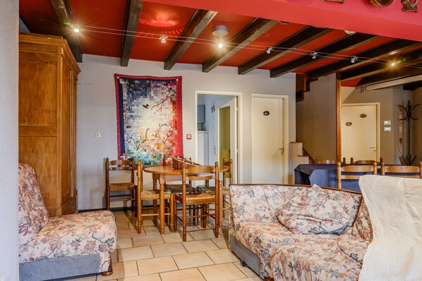 A living room with a dining table, chairs, a sofa, and a large tapestry on the wall. - Holiday Home 'Sur La Route Du Vin' with Balconies and Wi-Fi (Bergheim)